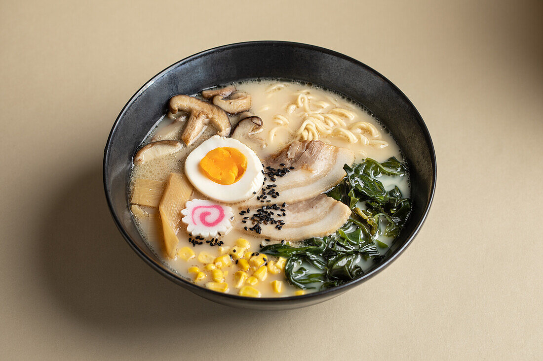 Appetitliche japanische Ramen mit gekochtem Ei und Pilzen in einer Schüssel vor beigem Hintergrund