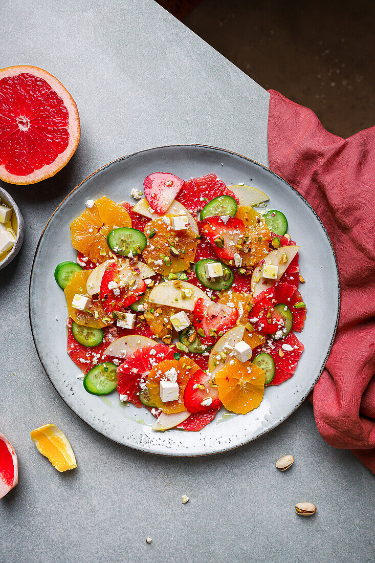 Draufsicht auf gesunden Salat mit Orangen, Erdbeeren, Äpfeln und Gurken, serviert mit Käse und Pistazien auf einem Teller