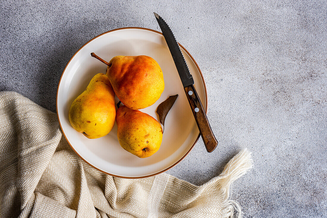 Von oben Keramikschale mit Bio-Birnen Obst in der Nähe von Messer auf Betonoberfläche