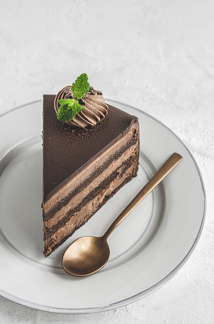 From above piece of yummy sweet chocolate cake decorated with cream served on ceramic plate with golden spoon on white tablecloth