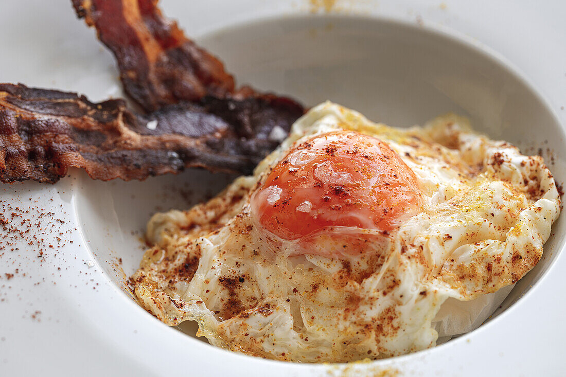 Overhead view of tasty eggs with fried bacon strips on plate