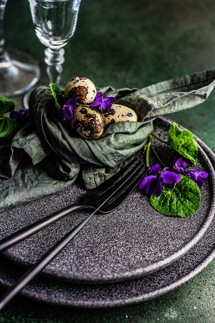 Frühlingshaft gedeckter Tisch mit blauer Viola-Blüte auf schwarzem Tellerset