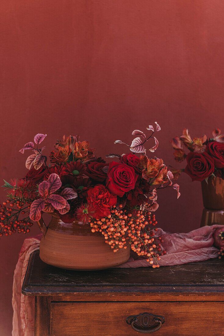 Eleganter Strauß frischer, üppiger roter Rosen und Lilien mit Zweigen roter Beeren in der Nähe von Stoff