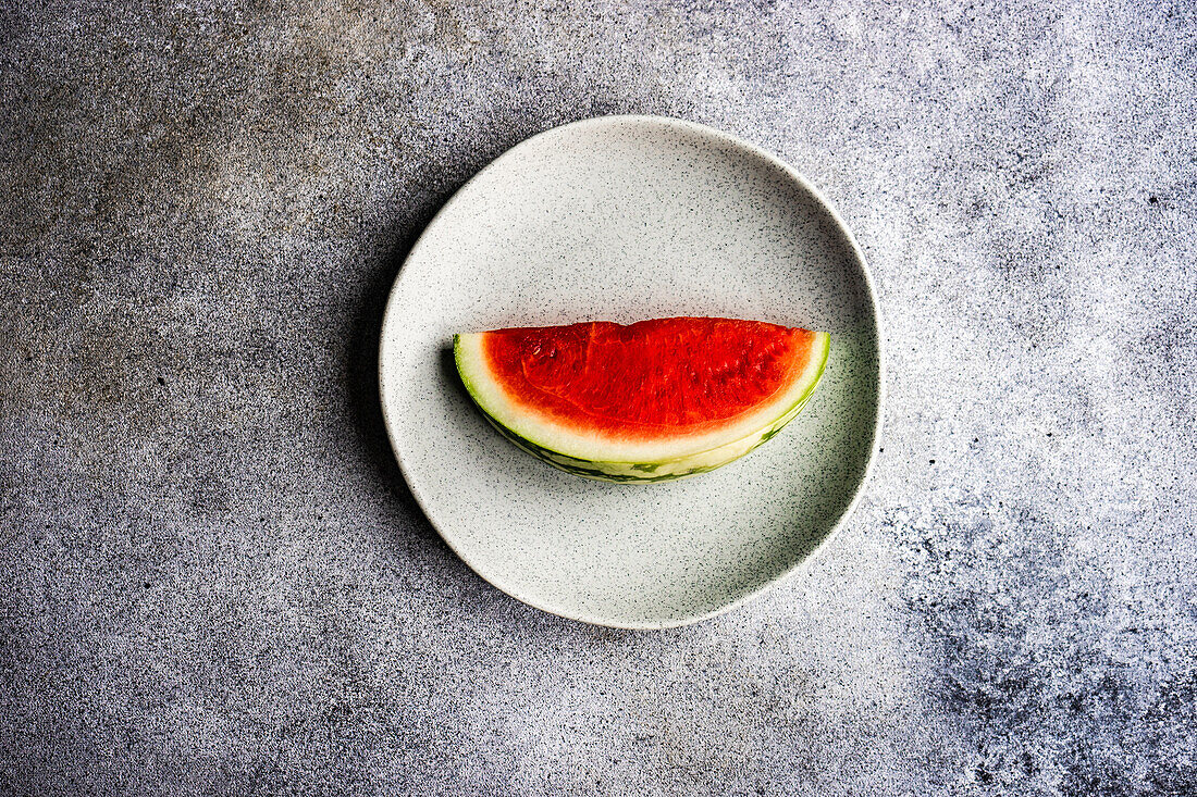 From above still life composition of sliced ripe striped green watermelon placed on stone plate on concrete background