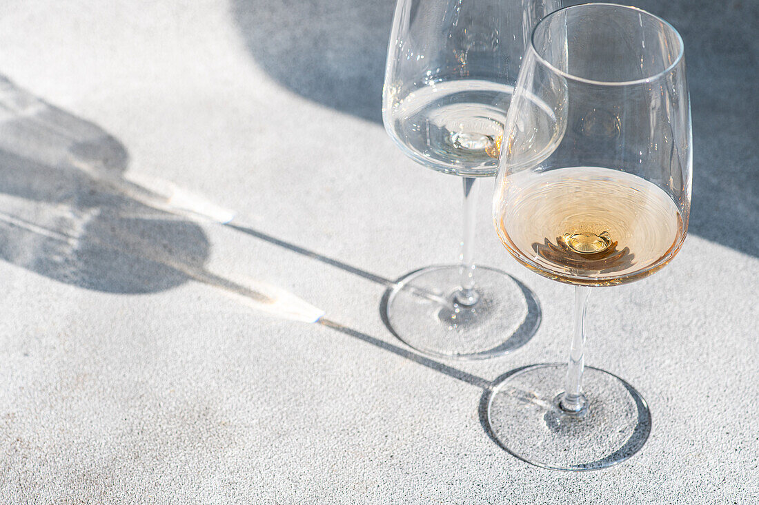 Pair of wine glasses with different kinds of dry white wine on grey concrete background with deep shadows