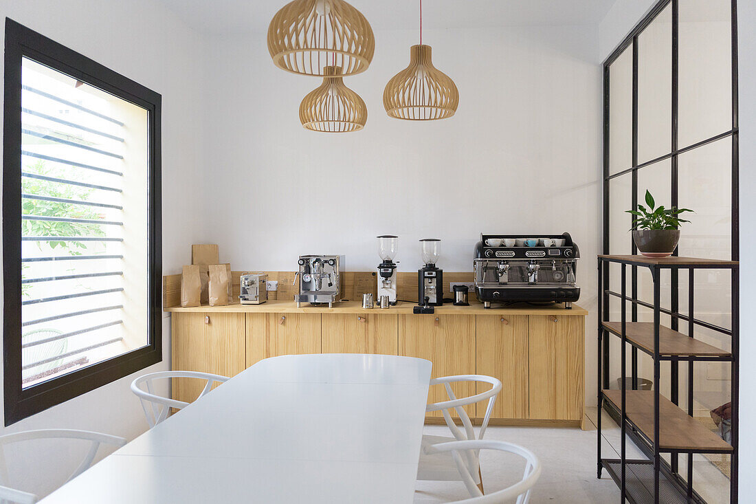 Modern coffeemaker machines and coffee grinders placed on wooden counter in light modern coffee house with white table near window and wooden shelves