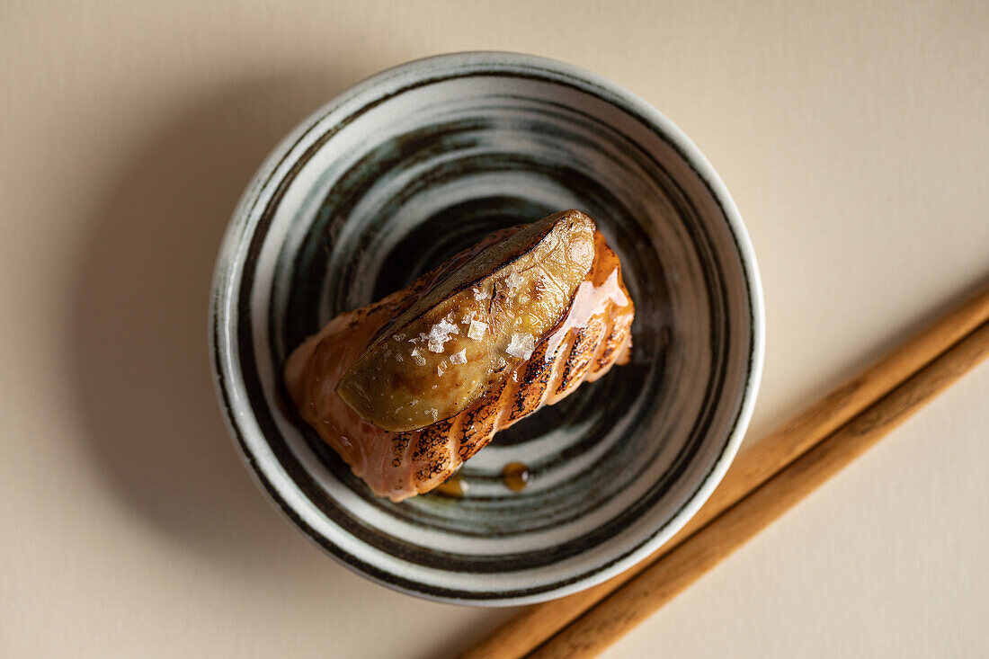 Draufsicht auf leckere japanische Nigiri-Sushi mit geräuchertem Lachs und flambierter Gänseleber, serviert auf einem Teller mit Stäbchen in einem Restaurant
