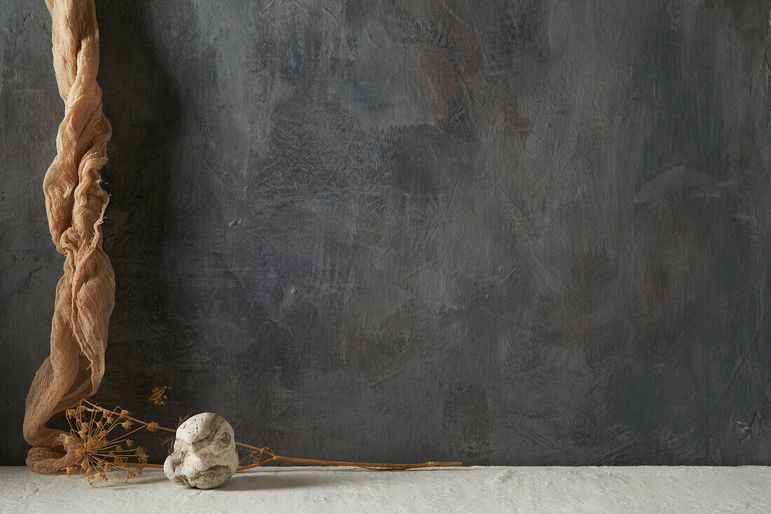 Stein und Stück Stoff mit getrockneter Pflanze auf beigem und grauem Hintergrund