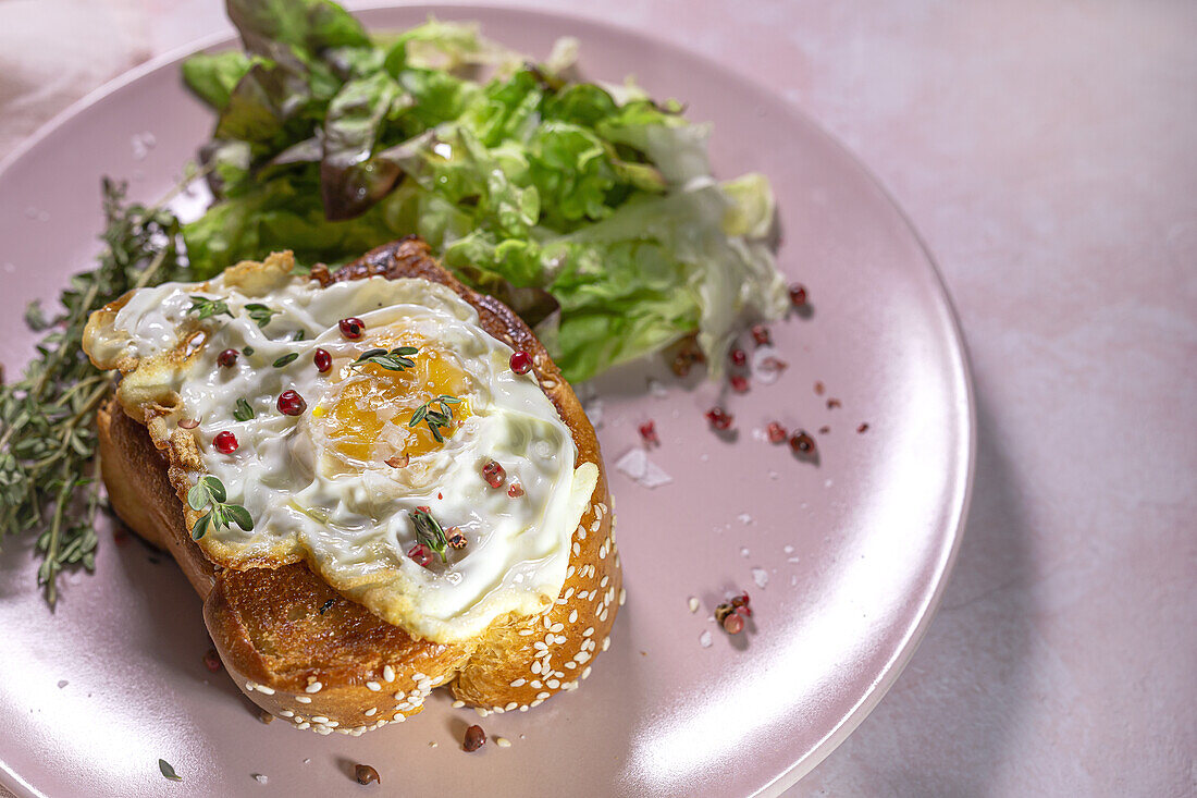 High angle of fried egg on brioche served on plate with fresh lettuce for appetizing breakfast on pink background