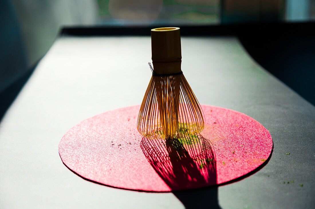 Bamboo chasen and powdered dried matcha on pink circle on black table in sunlight