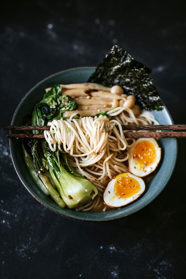 Top view of ceramic bowl with delicious ramen and chopsticks placed on table