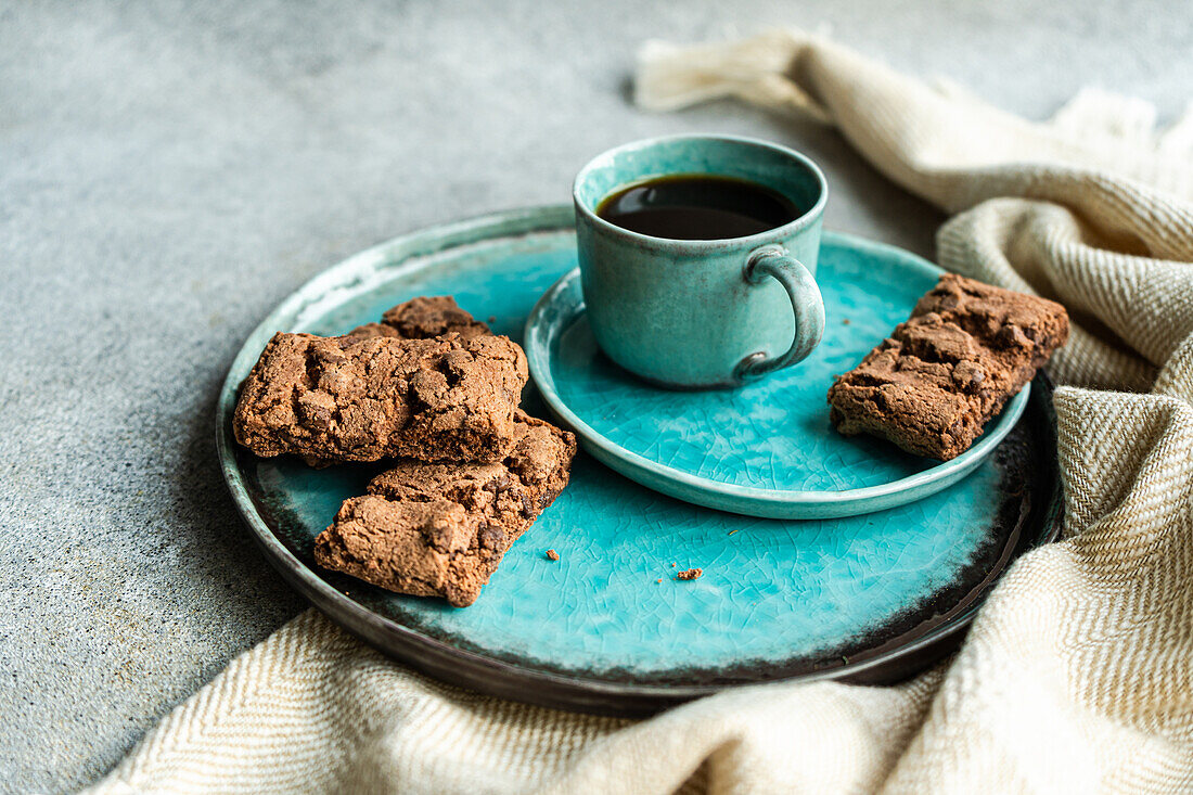 From above ceramic plate with fresh baked chocolate cookies near black coffee drink in a mug on concrete background