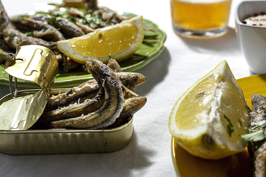 From above of delicious fried anchovies served on plate and cat with lemon and placed on white table with glass of beer
