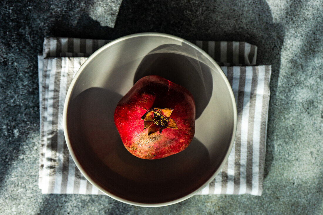 From above ripe organic pomegranate fruit on the ceramic bowl and tea towel