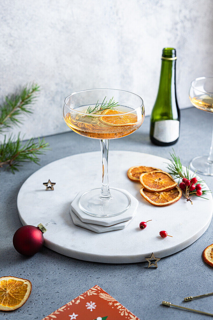 Blick von oben auf einen gedeckten Weihnachtstisch mit einem Cocktailglas mit getrockneten Orangen und Sekt