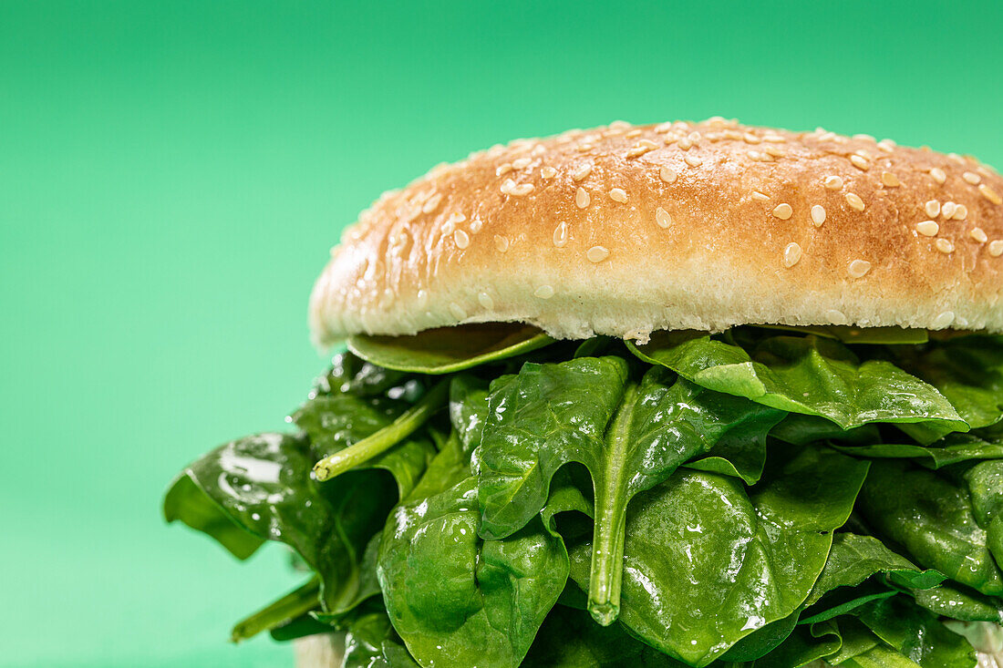 Fresh burger bun with bunch of fresh spinach leaves as concept of healthy food against green background