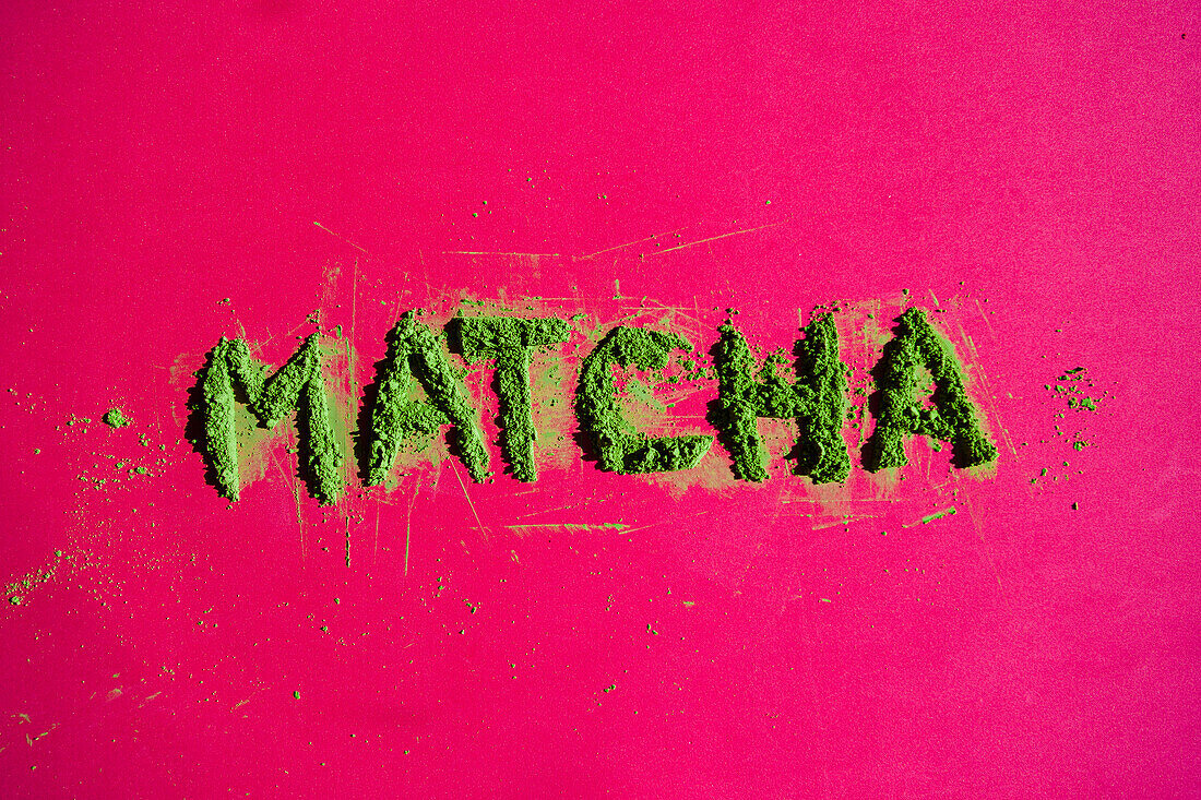 Draufsicht auf die Aufschrift Matcha aus getrockneten Grünteeblättern auf leuchtend rosa Hintergrund