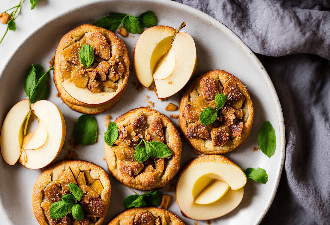 Top view of appetizing sweet baked mini apple pies served on white plate with fresh apples and mint leaves