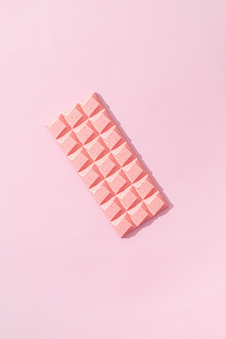 Top view minimalistic composition with pieces of handmade pink chocolate bar on pink background