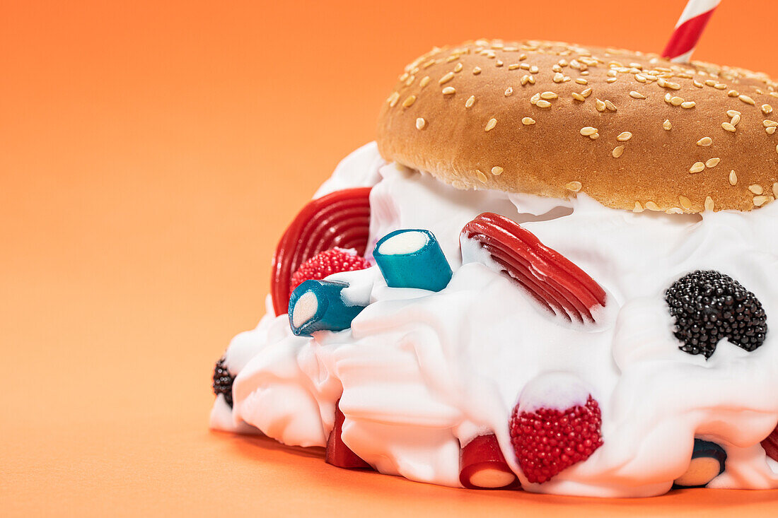 Fresh burger bun filled with sweet whipped cream and assorted jelly candies against orange background