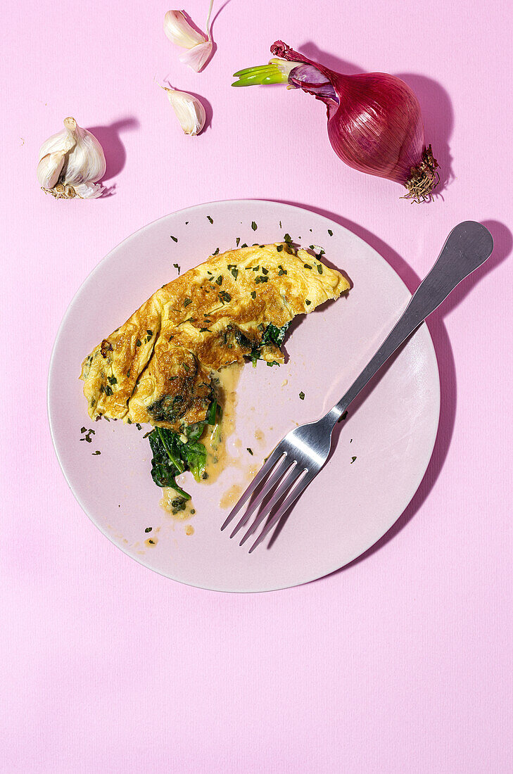 Tasty omelette on plate against fresh parsley sprigs and red onion with garlic cloves on pink background