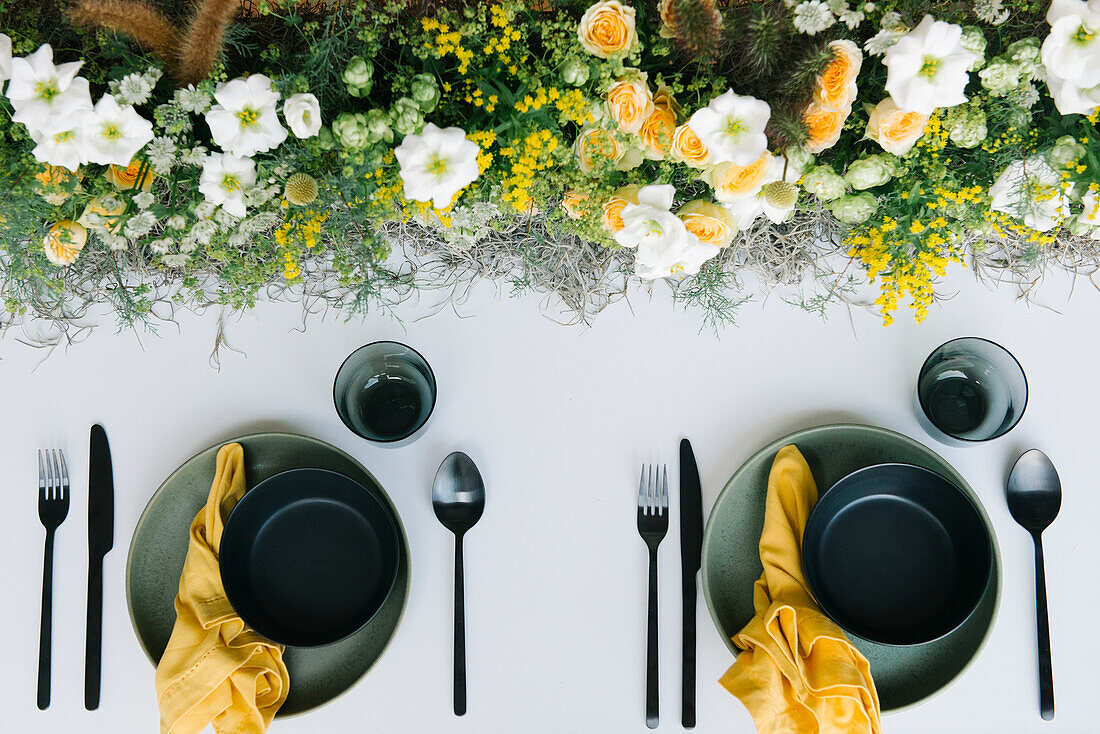 Top view of plate and bowl with cutlery and napkin served on table decorated with gentle fresh white and yellow flowers