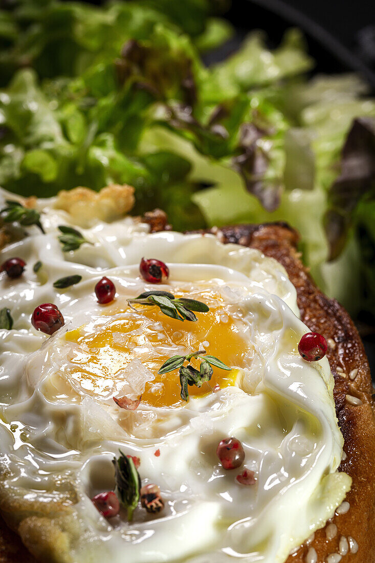 Fried egg on brioche served on tray with fresh lettuce for appetizing breakfast on black background