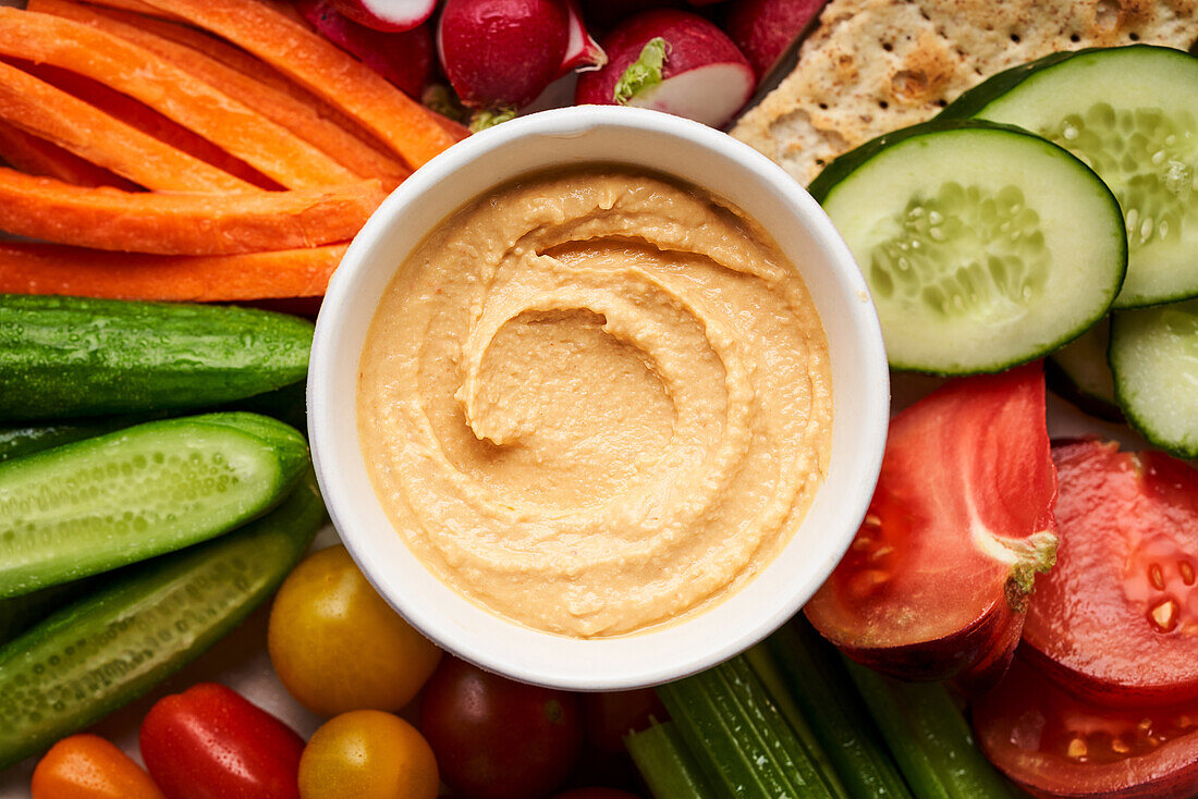 Top view bowl of homemade hummus served on plate with assorted fresh colorful vegetables