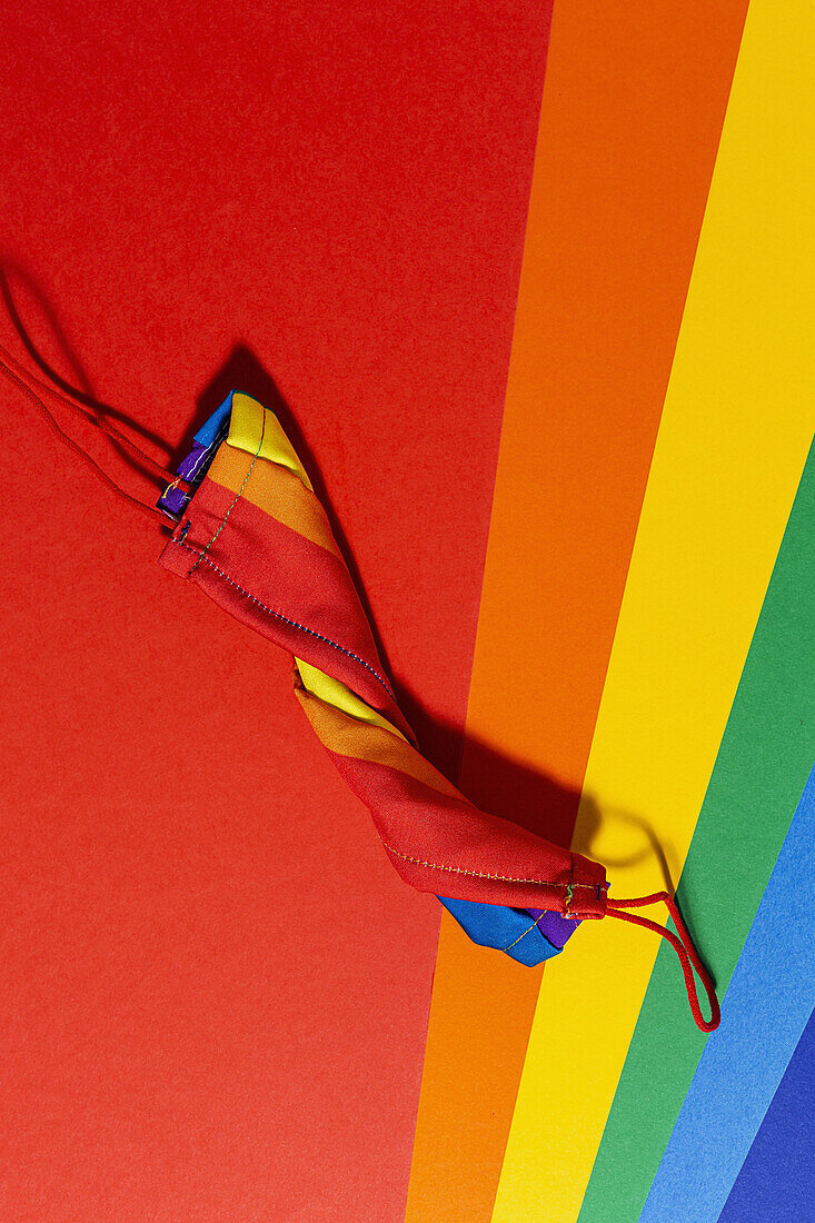 Ansicht von oben auf eine helle Gesichtsmaske aus gedrehtem Stoff mit Regenbogenornament auf buntem Hintergrund