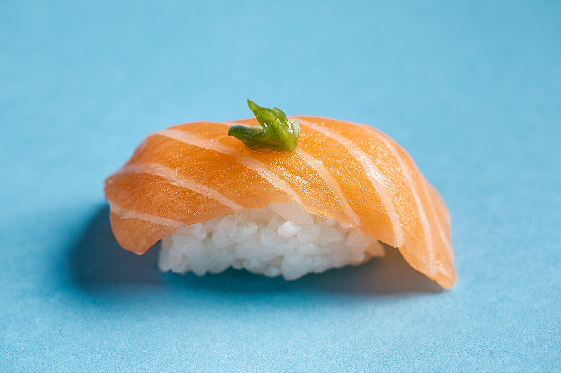 Tasty Japanese Norwegian nigiri with fresh salmon and spice green wasabi placed against blue background in light studio