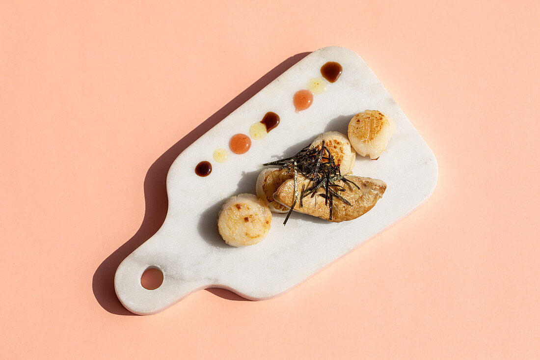 From above of tasty fried scallops with foie gras served on marble cutting board with colorful sauces