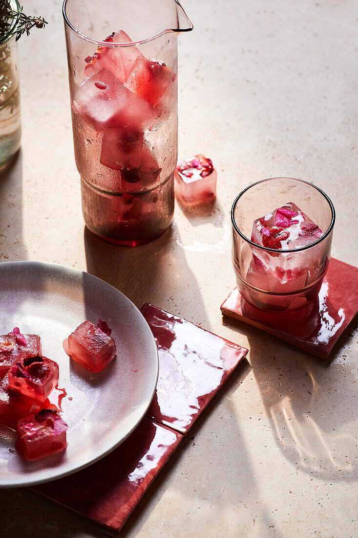 Von oben auf leckeres frisches Kaltgetränk aus gefrorenen Würfeln mit roten Blumen und Kräutern im Glas serviert