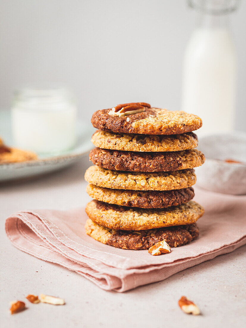 Stack of tasty cookies with walnuts placed on napkin on table against blurred bottle of milk
