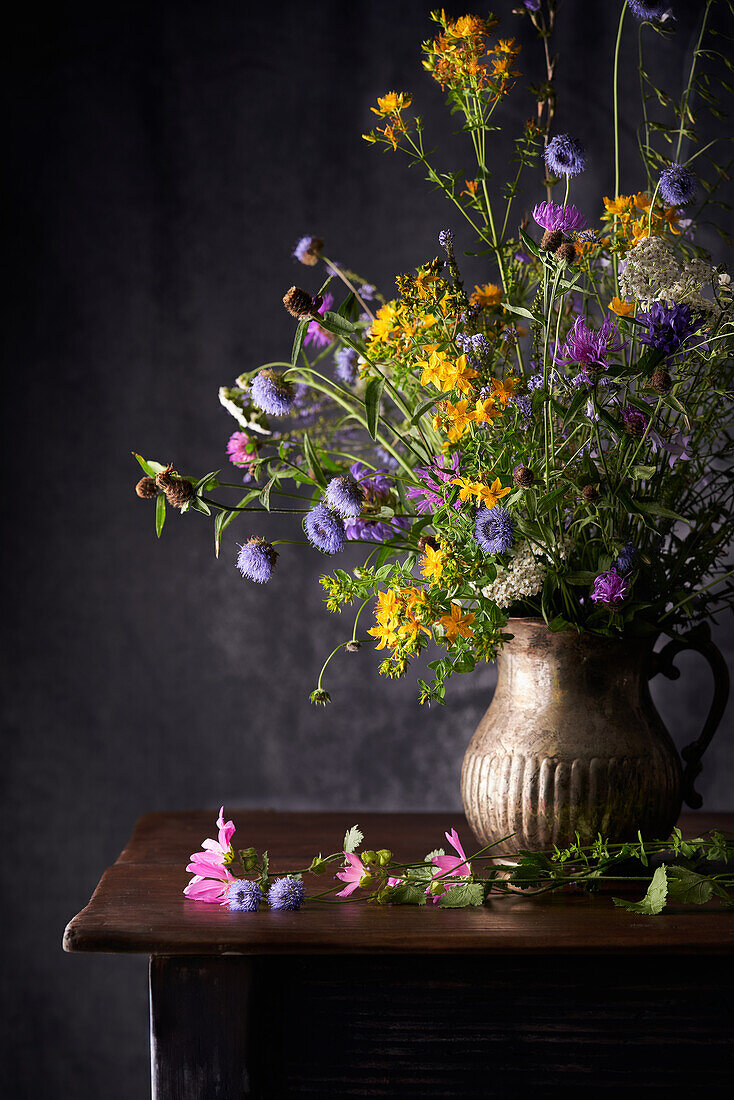 Bunte blühende Blumen auf dünnen Stielen in einer Vase auf einem Holztisch in einem Haus auf grauem Hintergrund