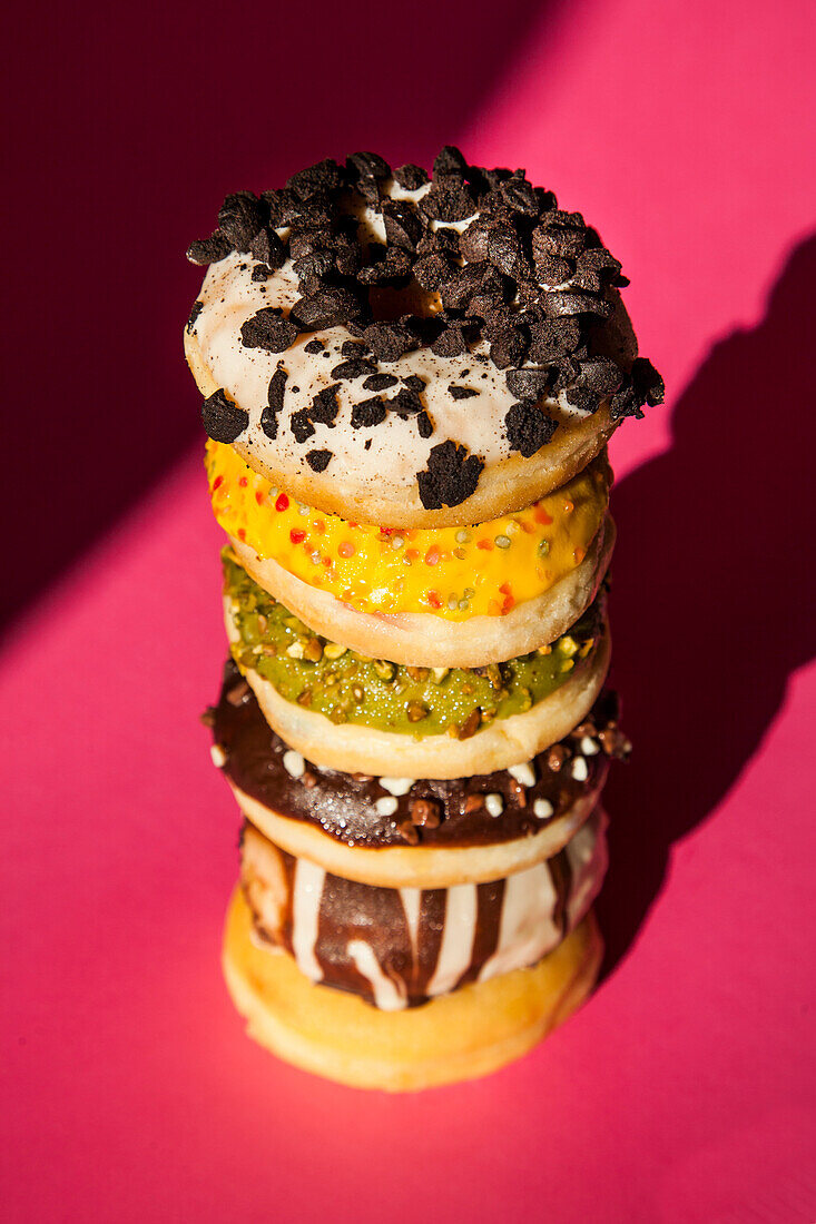 From above tower of donuts of different colors and flavors on pink background