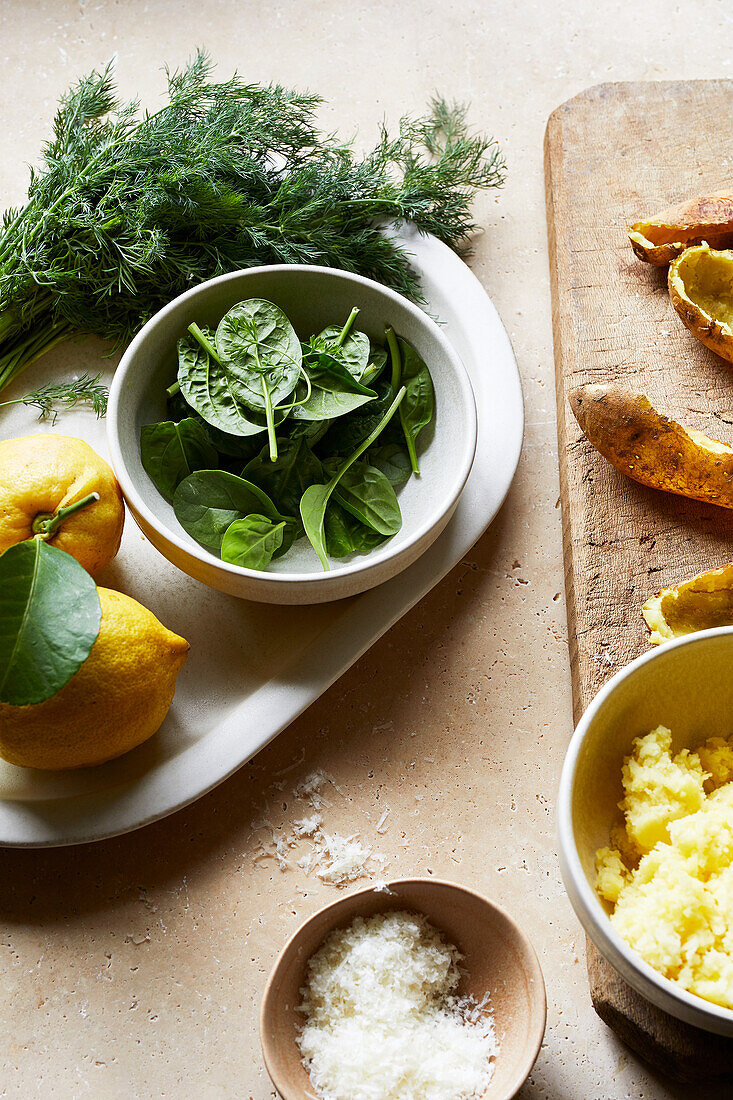 High angle of delicious fresh green spinach in bowl placed near lemons and mashed potato for gnocchi preparation