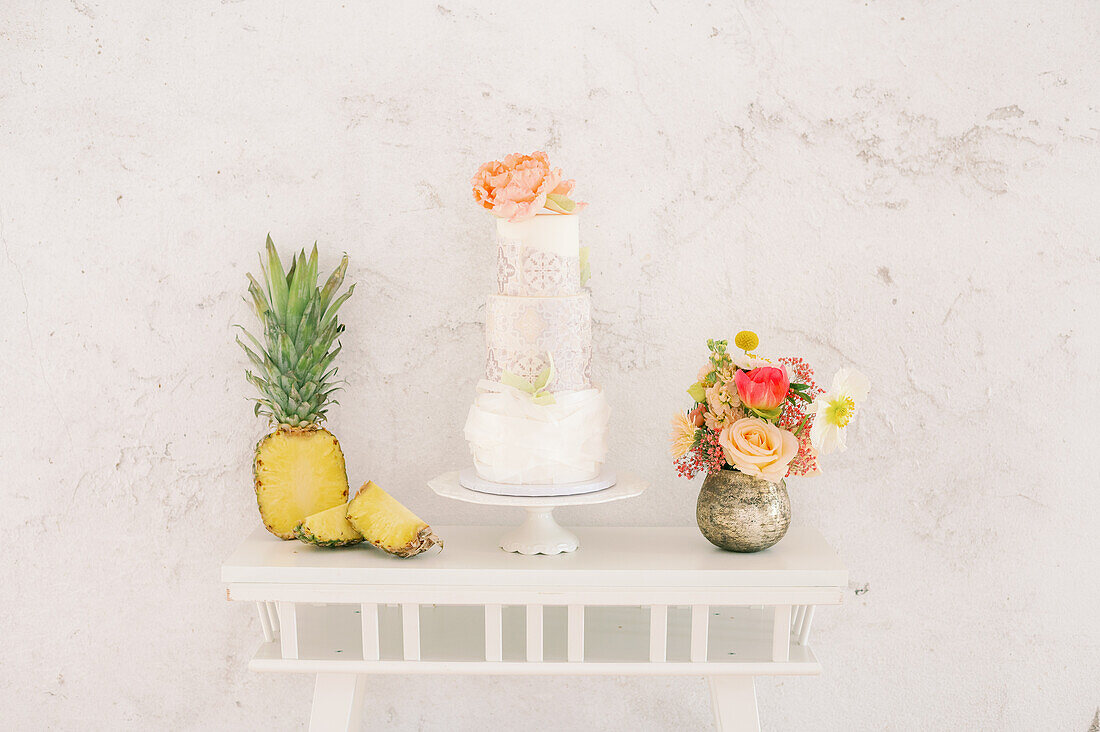 Fresh pineapples and tasty cake placed on table near red high heeled shoes against white wall during wedding celebration