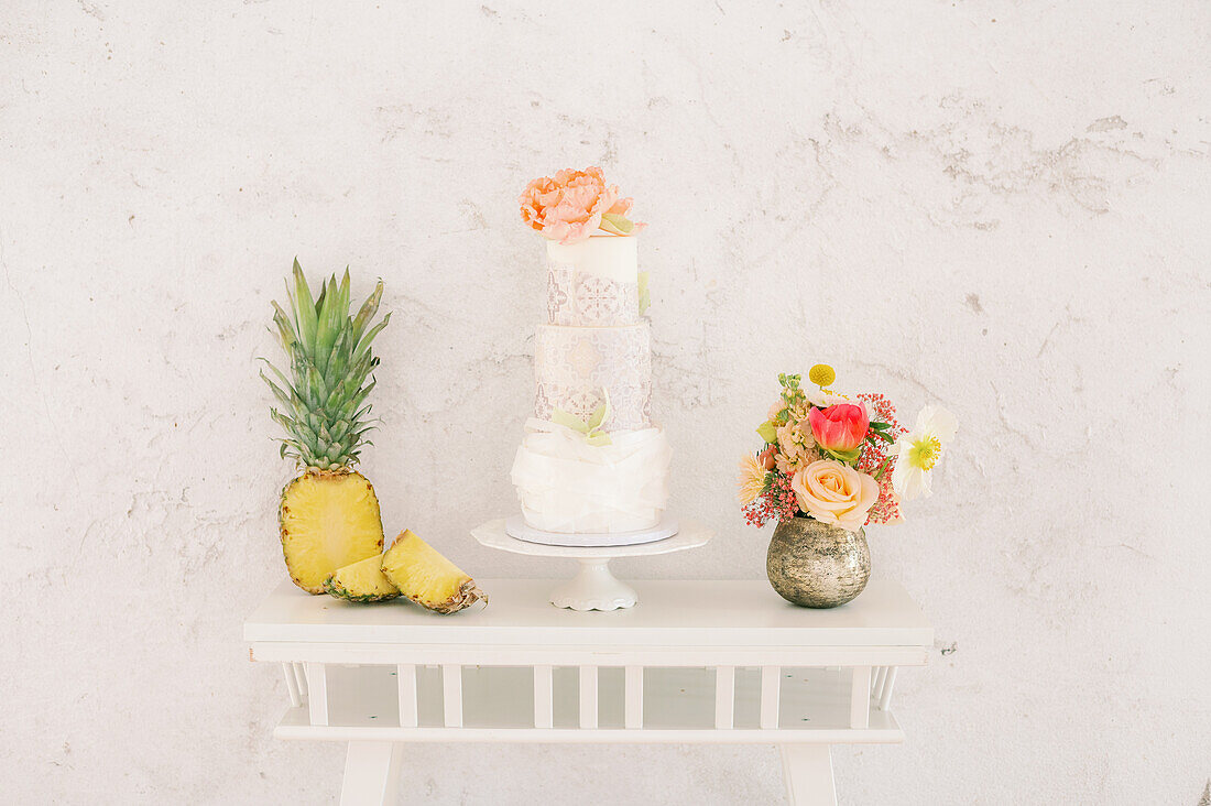 Frische Ananas und leckerer Kuchen auf dem Tisch neben roten hochhackigen Schuhen an einer weißen Wand während einer Hochzeitsfeier