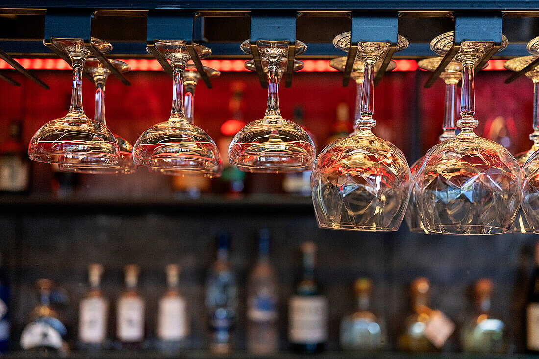 Various clean crystal glasses of different shape and size hanging on shelves over counter in bar