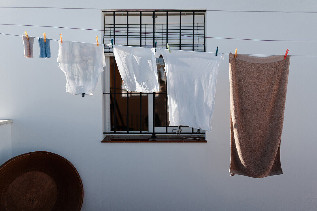 Gewaschene Wäsche hängt auf der Wäscheleine im Hof eines Landhauses mit weißen Wänden und Gitterfenster