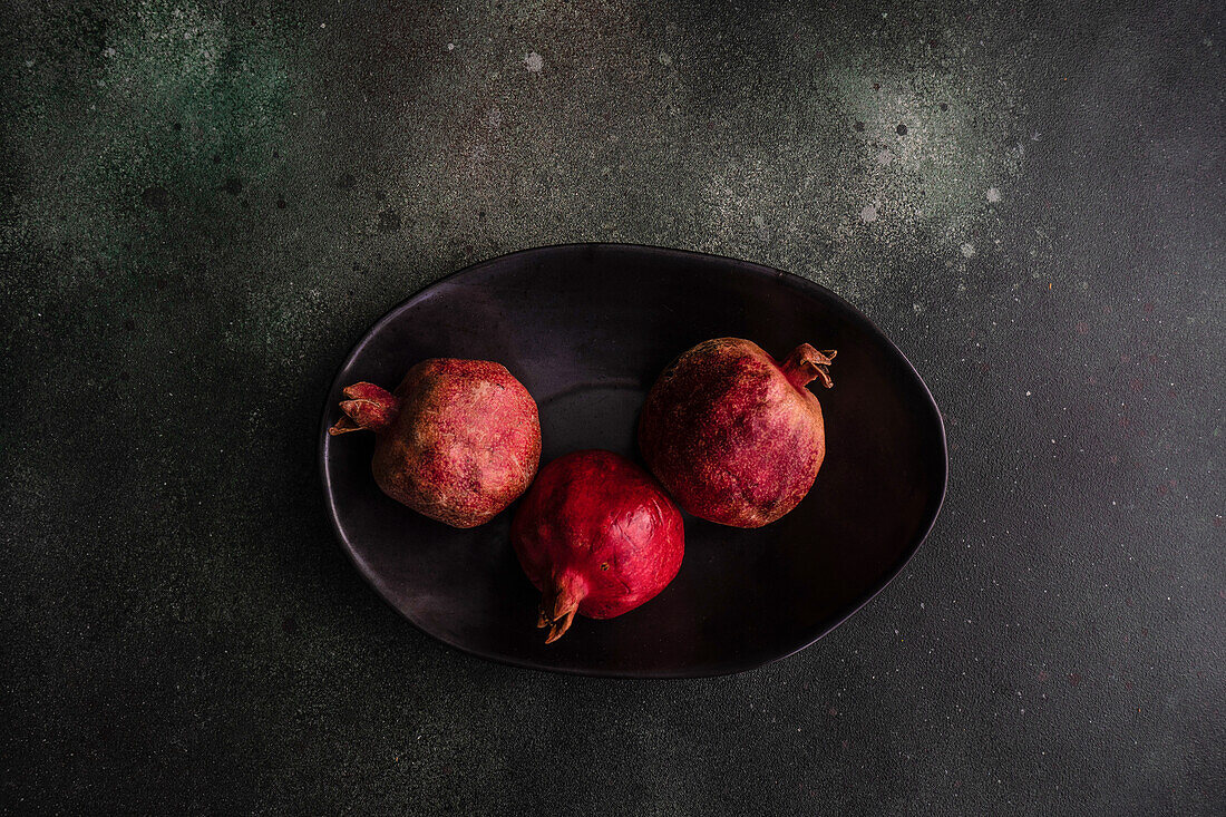 From above organic whole pomegranate fruits with its seeds on black stone background