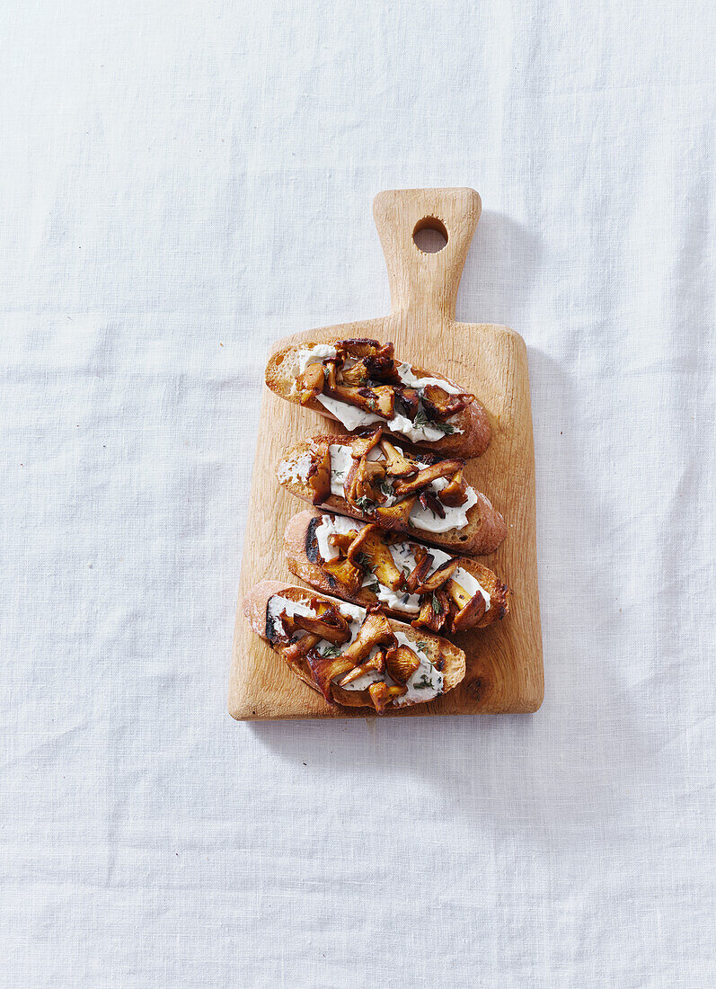 Bruschetta with chanterelle mushrooms and cream cheese served on a small wooden cutting board