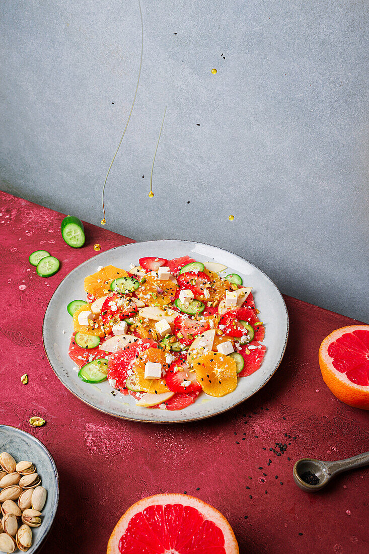 Draufsicht auf gesunden Salat mit Orangen, Erdbeeren, Äpfeln und Gurken, serviert mit Käse und Pistazien auf einem Teller