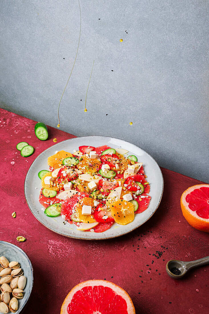 Top view of healthy salad with oranges and strawberries and apples and cucumbers served with cheese and pistachios on plate