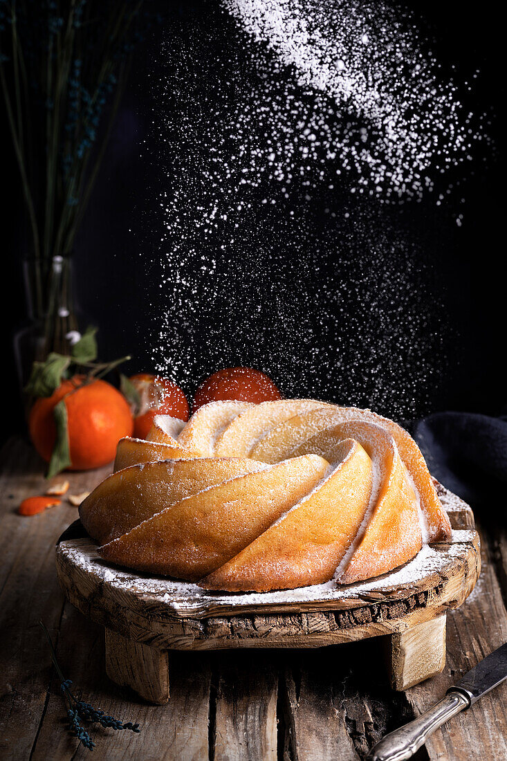 Appetizing sweet homemade bundt cake sprinkled with white sugar powder served on rustic wooden table with fresh tangerines