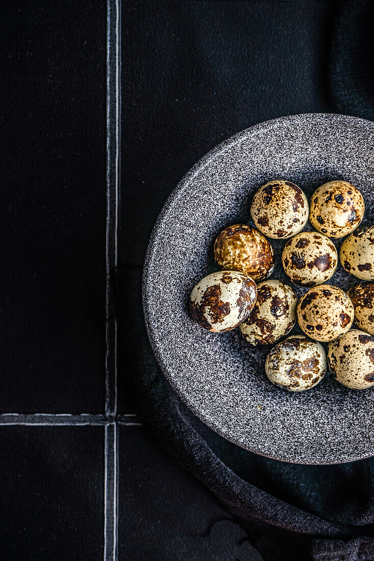 From above ceramic bowl with raw quail eggs on tiled table