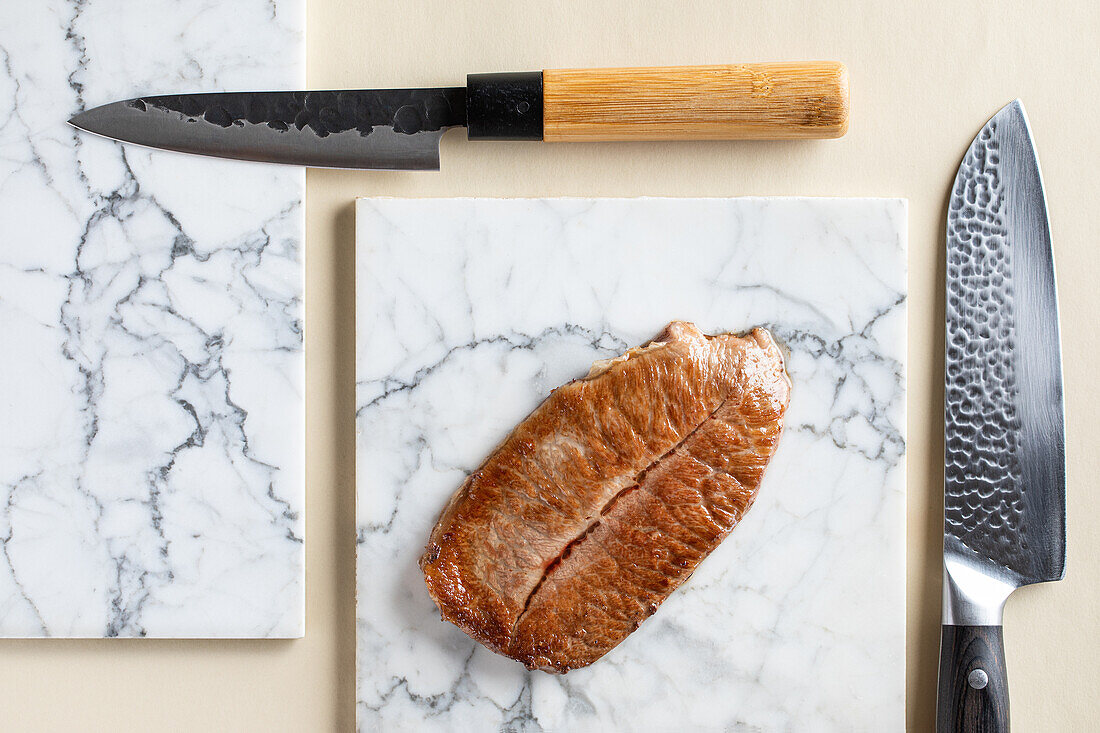 Top view of tasty kobe prefecture wagyu beef served on marble cutting board near sharp knifes in light kitchen during cooking process