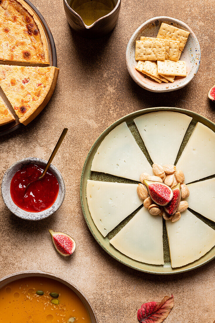 Top view of fresh cheese served on plate with nuts and fig near pumpkin soup and pie with crackers and sauce on table