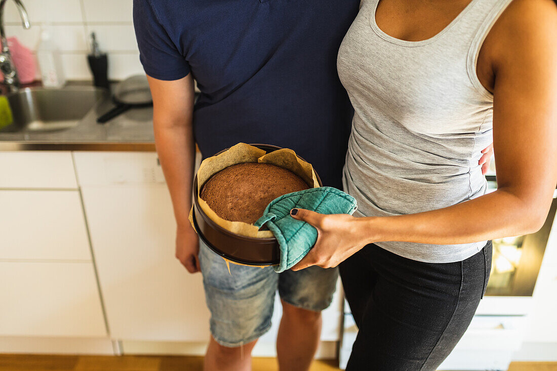 Anonymes multiethnisches Paar steht mit heißem, selbstgebackenem Kuchen in einem Bauernhof mit Pergament in der Küche