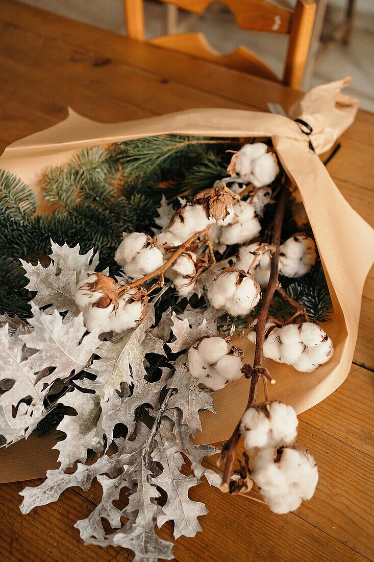 Festlicher Weihnachtsstrauß mit Baumwoll- und Tannenzweigen auf einem Holztisch im Zimmer